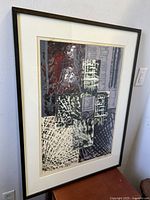 Full view of the framed abstract serigraph artwork displaying layered geometric shapes and textured patterns in mixed tones, placed against a white wall.