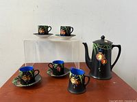 Full set displayed on clear risers showing coffee pot, creamer, 4 cups on saucers and 2 additional cups and saucers on raised platform