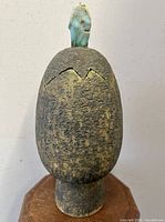 Front view of the oviform pottery vessel showing textured dark brown body and turquoise crackled glaze finial on lid.