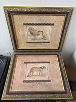 Pair of framed wildlife art prints shown, one featuring a lion and the other a cheetah, both in textured beige background frames with decorative borders.