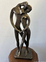 Front view showing the nude couple sculpture with flowing intertwined bodies and open spaces between figures on a wood stand.