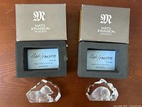 Two Mats Jonasson Sweden boxes containing glass paperweights, with the blue certification labels visible inside the boxes.