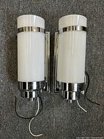 Two matching Art Deco style white glass cylindrical wall sconces with chrome metal mounts and accents, placed side by side on carpet.