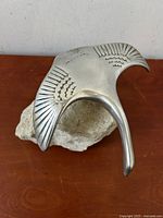 Front and top view of the stylized metal Canada goose sculpture with engraved feather details mounted on a rough natural rock base against a plain background.