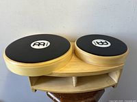 Front top-down view showing both round drums connected on a wooden bridge with Meinl logos on black drum heads.