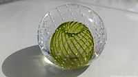 Front view of clear glass paperweight displaying central green swirl and bubbles.