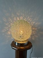 Lamp lit on a wooden stand showing the spaghetti style textured glass globe casting artistic light shadows on wall.