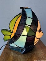 Side view of stained glass angelfish table lamp showing yellow and green glass fins, orange, black, white and blue glass sections.