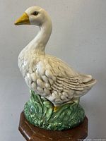 Front angled view of the ceramic duck statue showing detailed feather design and green grassy base