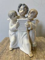 Front view of the porcelain Lladro choir of angels sculpture showing three angels around a music sheet with detailed facial expressions and robes.