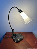 Front view of the working table lamp turned on, showing the frosted white art glass shade and curved stem on a wooden table.
