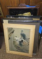 Stack of framed artworks with wooden tray visible at back