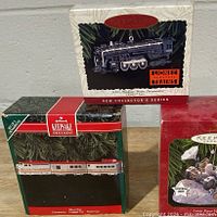 Front view of three boxed ornaments: steam locomotive, passenger railcar, lunar rover