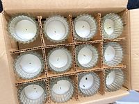 Open carton showing grid with multiple paneled glass votive holders containing used candles