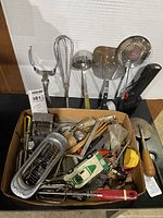 Box with assorted kitchen utensils plus loose large utensils at back