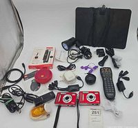 Lot overview showing cameras, speaker, tablet, flashlight, remote, cables and adapters