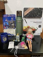 All lot items group shot showing thermos, fondue maker, curling iron, boxed truck bank, action figure, Barbie, figures, mug