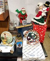 Group shot showing all holiday collectibles including plates, glass mug, Santa figurine, dolls, bear figurine