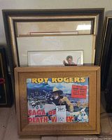 Stack of framed items with Roy Rogers clock in front and other prints behind