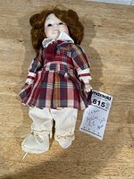Full view of doll with plaid outfit, pantaloons, single shoe, lot tag visible