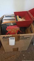 Cardboard box containing LP records and red plastic carrying box