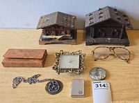 All items laid out including two chalet music boxes, Dior case, ornate clock, eyeglasses, necklace, Zippo lighter, button