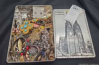 Open tin showing assortment of costume jewelry pieces and tin lid design