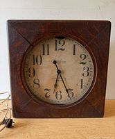 Front view of square wood wall clock showing full dial and case