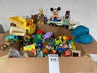 Cardboard box filled with mixed toys including Tonka dump truck, Hess truck with Mickey Mouse, Donald Duck, vehicles, figures and teal hair pieces
