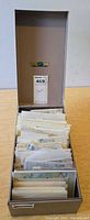 Open metal file box filled with rows of glassine envelopes containing stamps