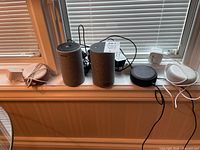 Five Amazon smart speakers on a windowsill. Two Echo Plus devices with fabric finish, three smaller Echo Dot 3rd gen devices in black with their power adapters and cables. Untested condition.