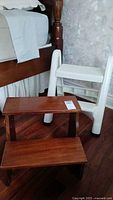 Mahogany bed steps in front of bed next to white Rubbermaid foldable foldable step stool.