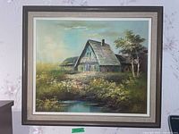 Full view of the framed original painting showing a rustic cottage near a pond with natural surroundings.