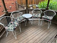 Full set of four white cast metal chairs with cushions and round side table arranged on a deck.