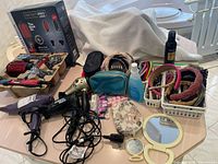 Full view of all hair care accessories spread on table including Conair InfinitiPro 1000 watt dryer brush box, 2 hair dryers, headbands, toe spacers, mirrors, and hair spray.