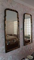 Two rectangular Chinoiserie-style wall mirrors with black and gold frames hung on floral wallpaper.