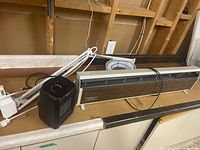 General Electric 1500 watt baseboard heater, small black portable space heater, and white clamp magnifying lamp all on a workbench surface in basement