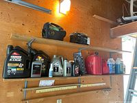 Shelf with automotive fluids and accessories including Castrol Edge motor oil (5L), smaller oil containers, two red gas cans, windshield washer fluid, car fresheners and black battery charger box