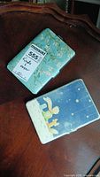 Two Kindle covers on wooden surface, one floral design, one Little Prince design