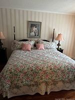 King size bed made with floral bedding, two pink pillows and two floral pillows, and visible headboard with dark wood finish.