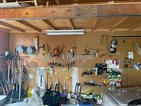 Wide view of the pegboard wall in garage with hanging wrenches, sockets, hand tools, rakes, and other gardening tools stacked and arranged.