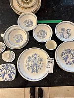 Photo showing assortment of plates and bowls with blue floral and character patterns in folk art style from Lotte China, including small mug and covered dish.