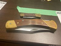 Two vintage folding pocket knives with wood and metal handles, displaying both closed sides on a dark surface.