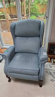 Front view of the powder blue manual recliner chair showing cushioned seat, backrest, armrests, and wooden legs.