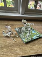 Clear Swarovski crystal rocking horse figurine on beveled display mirror next to seated ballerina figurine on wooden surface near window.