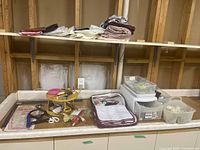 Wide view of a countertop with assorted sewing tools, scissors, electric glue gun, elastic bands, and storage containers with sewing supplies.