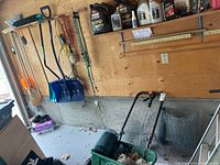 Photo showing green Scott's AccuGreen 3000 fertilizer spreader positioned on the floor with wheels, nearby rolls of chicken wire and burlap, and wall mounted shovels, brooms, ropes.