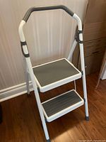 Front angled view of the Gorilla Ladders two foot step ladder showing the white metal frame and gray tread steps with padded handle.