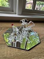 Two Swarovski crystal figurines on an octagonal mirror: a seated clown with colorful details and a seated jester with colored hat and shoe tips.