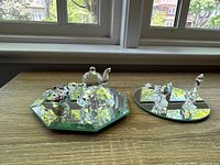 Full lot view showing all Swarovski crystal figurines arranged on two mirrored display plates on a tabletop by a window with natural light